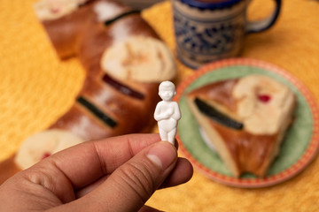Woman hand holding a baby Jesus figurine with traditional Epiphany cake and a mug out of focus