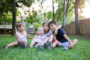 Naklejka na ściany i meble Three young boys and toddler girl in summer park