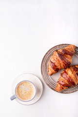 Croissants and a cup of coffee on a white wooden table. Morning still life. Top view with space for text. Flat lay composition. Background for restaurant, bakery, cafe.