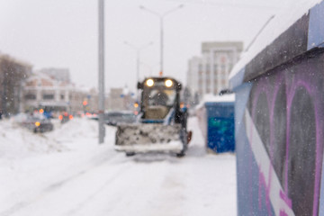 blurred background - city during snowfall and snow removal loader
