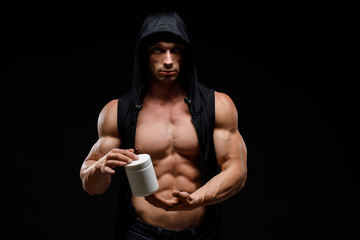 Muscular bodybuilder with jar of protein on a dark background. Sports nutrition. Bodybuilding nutrition supplements, sport, workout, healthy lifestyle concept.