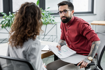 selective focus of account manager holding papers and talking with colleague