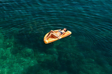 Slim young woman in bikini and sunglasses on the air mattress floats in the open sea.