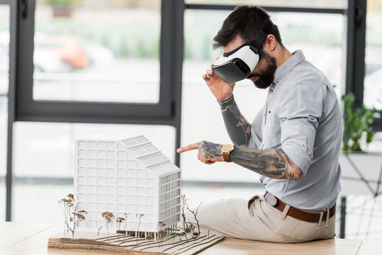 virtual reality architect in virtual reality headset pointing with finger at model of house - Powered by Adobe