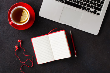 Blank red notebook, computer laptop, headphones and cup of tea.