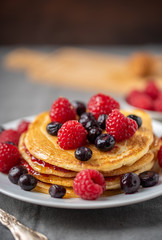 Sweet homemade pancakes with raspberries and blueberries on white plate.