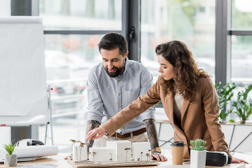 smiling virtual reality architects talking and pointing with finger at model of house