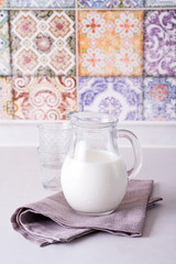 fresh milk in glass jug and glass on stone table on the background of the old colored kitchen tiles