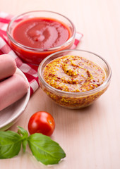 Bowls with ketchup and dijon mustard close-up and milk sausages on a background.