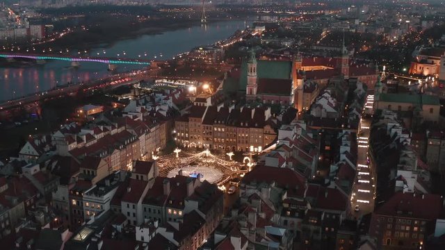 Drone flies over the old buildings of the old city in the Royal Palace at dusk with New Year's lighting and a Christmas tree on the square. Warsaw, Poland.