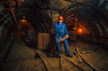 A miner in a coal mine stands near a trolley. Copy space.