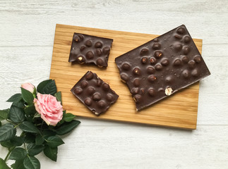  flat lay, broken chocolate bar on the wooden board and a pink rose