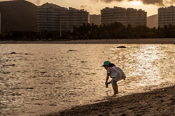 Girl in a in a colorful blouse plays with water on the beach during yellow sunset in the evening in...