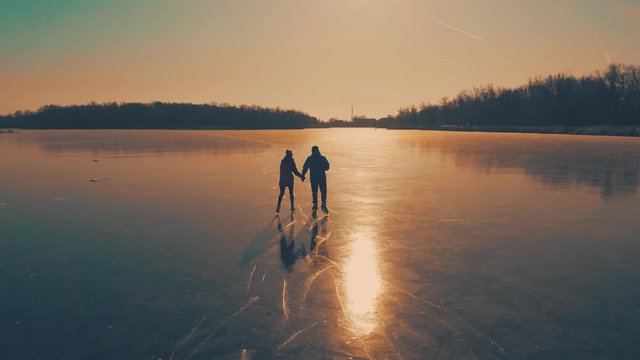 Happy couple ice skating outdoors on a frozen lake on a lovely sunny winter day. Ice skating lovely couple having winter fun on ice skates.