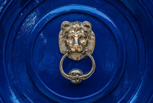 Classical European style brass lion head door knocker against a bright blue painted wooden door.