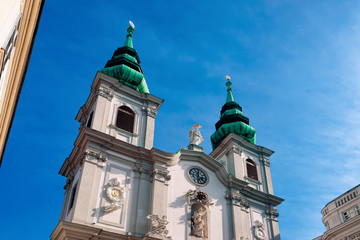 Fototapeta na wymiar Two towers of Church of Mariahilf on Mariahilfer Strasse Street in Vienna in Austria. Cathedral archtecture in Wien. Basilica Building landmark. Austrian town. Blue sky background