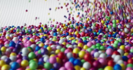 Multi-colored balls falling and scattering in different directions and rolling on a white surface