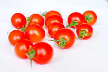 A few fresh red cherry tomatoes lie on a white background in random order. Selective focus. Close up.