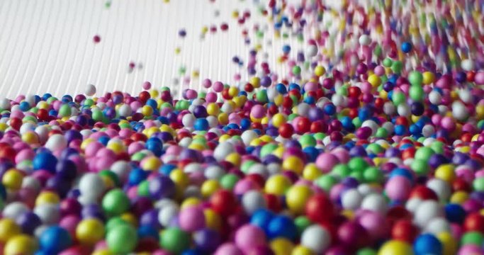 Multi-colored balls falling and scattering in different directions and rolling on a white surface