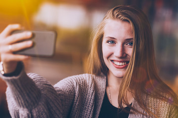 beauty asian girl smiling and showing smartphone with empty screen for your text in cafe background.Close-up photo of attractive smiling girl standing on grey background and holding smartphone