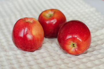 Three fresh red apples lie on a kitchen napkin on a white background. Selective focus. Close up.