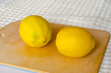 Two fresh yellow lemons lie on the cutting Board next to the kitchen napkin. Selective focus. Close up.