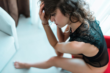Young sexy brunette woman in sexy black lace lingerie sitting on red sofa in luxury apartment