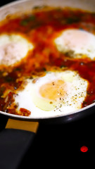Selective focus. Shakshuka cooked on a frying pan. Cooking Israeli Shakshuka fried eggs. Middle Eastern cuisine. Fried eggs in tomato sauce.