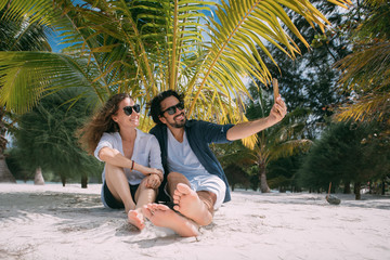 A pair of lovers take a selfie under a palm tree on a tropical beach