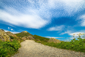 Ein Wanderweg bei sonnigem Wetter in den schweizer Alpen, mit leicht bewölktem Himmel