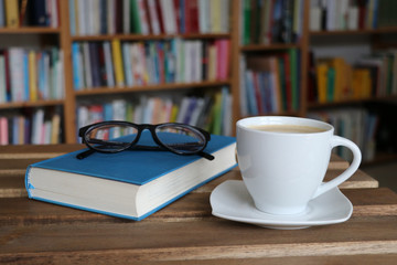 Kaffee, Cappuccino, Tasse, Buch mit Brille vor Bücherregal