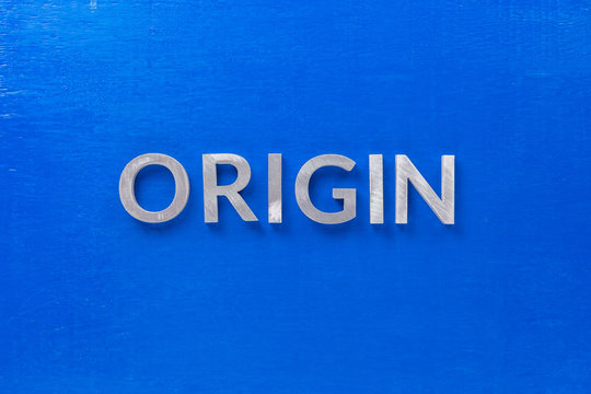 the word origin laid with silver metal characters on blue board in flat lay centered composition