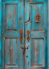 Splintered and peeling wooden turquoise door with rusted bell