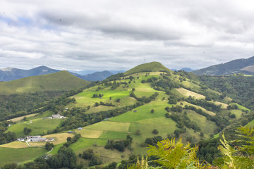Fototapeta premium View from the mountain. The top viewpoint. Forests and colorful fields. The nature of France. Walking in Europe. Green tourism. Panorama of green hills. Mountains in the clouds.