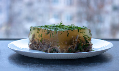 Russian aspic jelly with greens on a white plate.