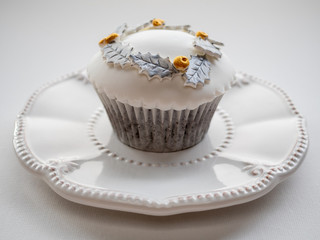 White cupcake with gold and silver decoration on white plate and  white background. Close up.