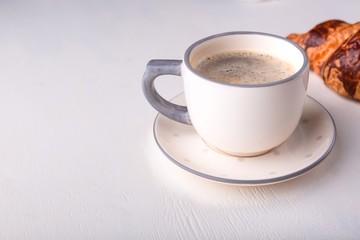 Croissant and a cup of coffee on a white wooden table. Morning still life. Banner for restaurant, bakery, cafe.