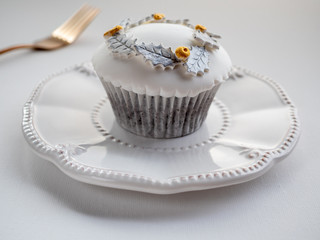 White cupcake with gold and silver decoration on white plate and  white background. Close up.