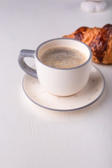 Croissant and a cup of coffee on a white wooden table. Morning still life. Banner for restaurant, bakery, cafe.