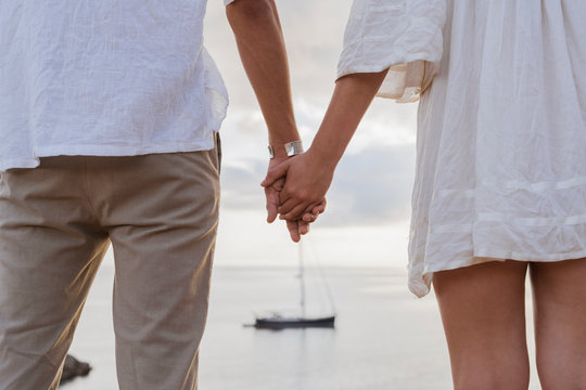 Back view of young couple in love standing in front of the sea holding hands
