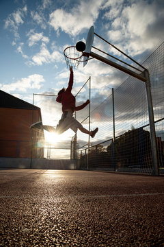 Teenager playing basketball, dunking against the sun