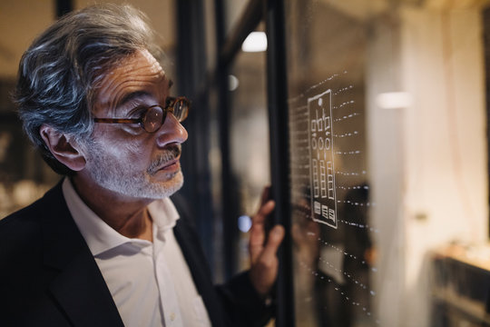 Senior businessman looking at drawing on glass pane in office