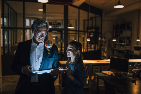Happy senior businessman and girl with hot-air balloon and shining tablet in office