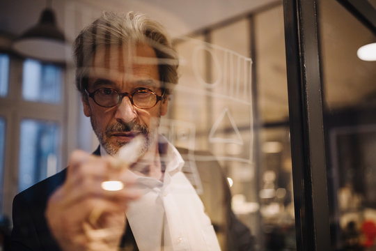 Senior businessman drawing on glass pane in office