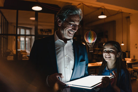 Happy senior businessman and girl with hot-air balloon and glowing digital  tablet in office