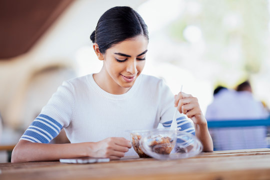 Young woman sitting at table eating takeaway food