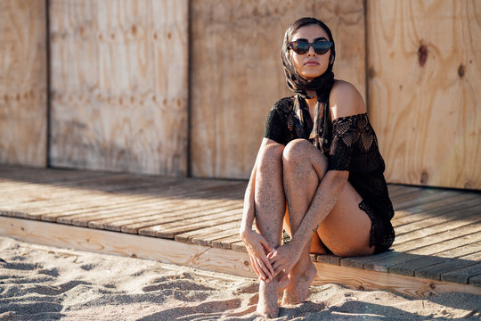 Young woman wearing headscarf and sunglasses sitting at the beach