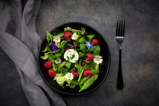 Bowl of fresh salad with arugula, spinach, chard, oak leaf, lollo rosso lettuce, corn salad, raspberries, cream cheese, chive and edible flowers