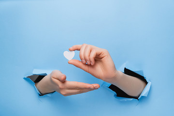 Female hand holding little white hearts through a torn blue paper wall. Valentines day and Like...