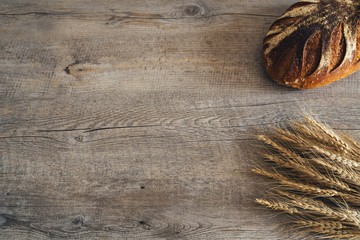 Rustic sourdough bread loaf and wheat on an old vintage planked wood table. Background with free text space.